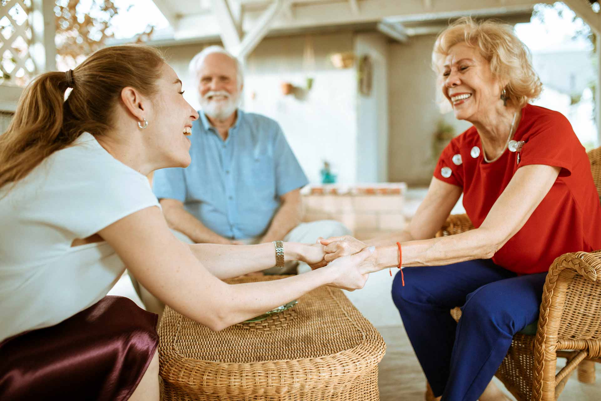 Young woman holding elderly woman's hands as they smile with one another.